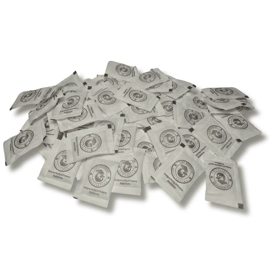 A large, scattered pile of white desiccant packets on a white surface. Every packet displays a circular logo of a mushroom and the brand name "Easy Mushroom Cultivation."