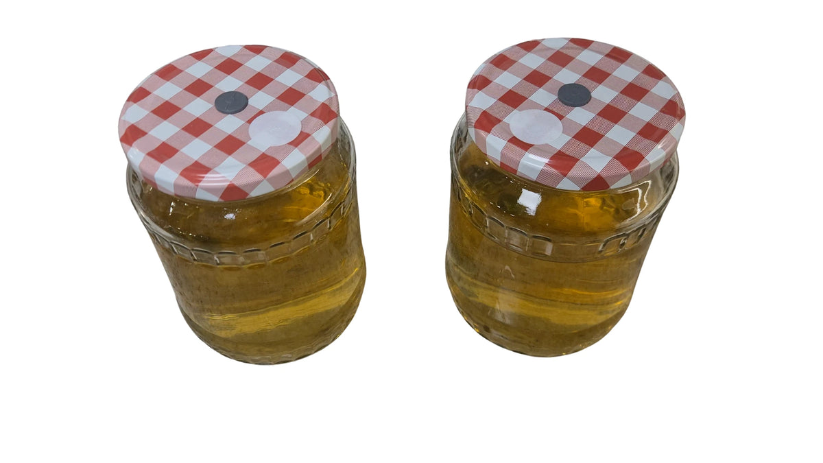Mushroom liquid culture kit: Two glass jars of golden nutrient broth with modified checkered lids.