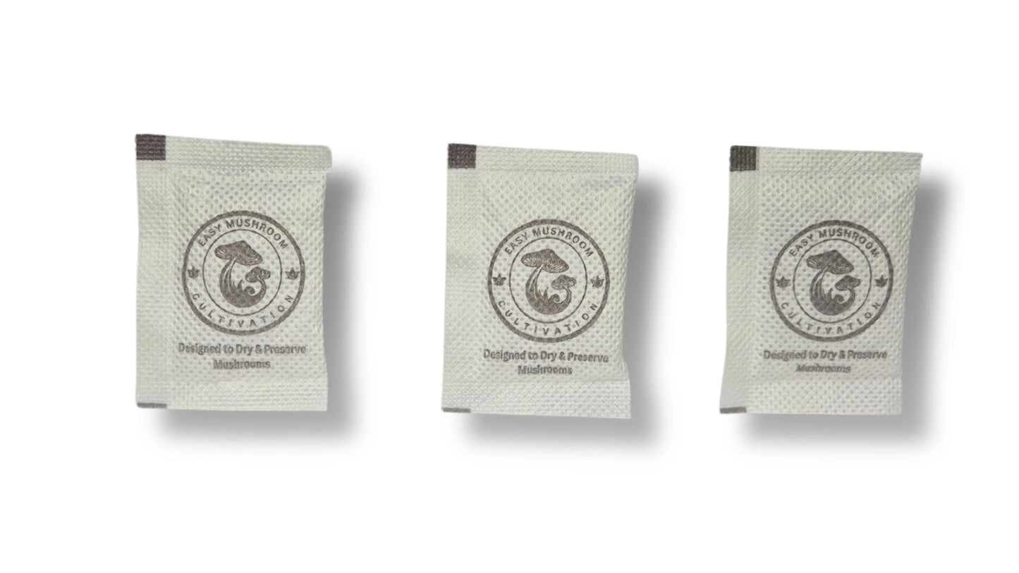 Three individual white desiccant packets arranged side-by-side against a white background. The packets are printed with a mushroom logo and instructions for drying and preserving mushrooms.