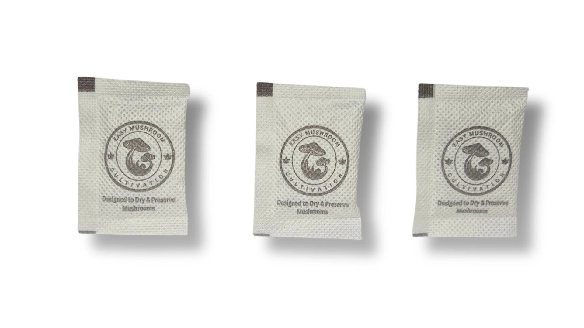 Three individual white desiccant packets arranged side-by-side against a white background. The packets are printed with a mushroom logo and instructions for drying and preserving mushrooms.